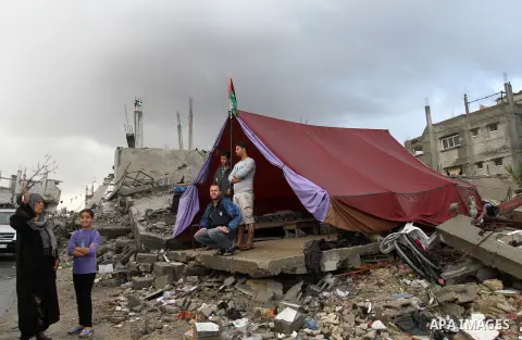 Palestinians stand outside a makeshift tent erected near the ruins of a house that witnesses said was destroyed by Israeli shelling during the most recent conflict between Israel and Hamas, on a rainy day in the east of...