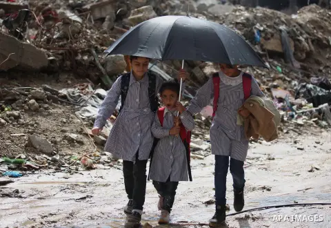 Palestinian students hold an umbrella as they walk past the ruins of a house that witnesses said was destroyed by Israeli shelling during the most recent conflict between Israel and Hamas, on a rainy day in the east of G...