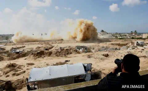 A Palestinian photographer takes photos as smoke rises after a house is blown up during a military operation by Egyptian security forces in the Egyptian city of Rafah, near the border with southern Gaza Strip November 3,...