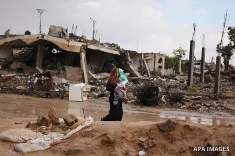 A Palestinian woman carries her daughter as she walks past a house, which witnesses said was destroyed by Israeli shelling during the most recent conflict between Israel and Hamas, following heavy rain in the east of Kha...