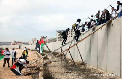 Palestinian and foreign activists use ladders to cross over the separated wall next to the Qalandia checkpoint, north of Jerusalem, 14 November 2014. Israel eased restrictions at Jerusalem's Al-Aqsa mosque after US Secre...