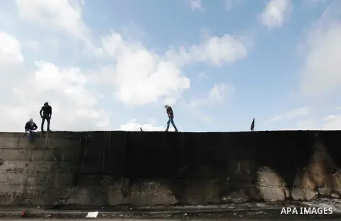 Palestinian protesters stand atop a section of Israel's controversial barrier that separates the West Bank town of Abu Dis from Jerusalem November 17, 2014. A Palestinian bus driver was found hanged inside his vehicle on...