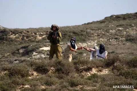 An Israeli soldier stands next to Israeli settlers throwing stones at Palestinian villagers during clashes in Oref village near Nablus City, 18 November 2014. Reports state that the clashes occured after a group of Israe...