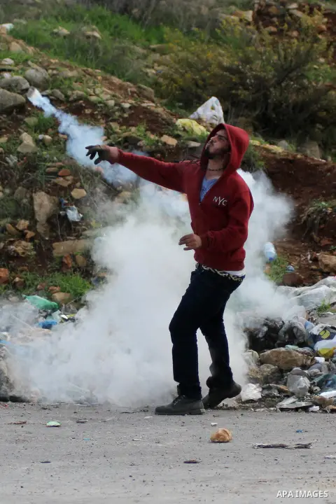 A Palestinian protester throws back a tear gas fired by Israeli security forces during clashes outside Ofer military prison, near the West Bank city of Ramallah, November 18, 2014. Two Palestinians armed with a gun and m...