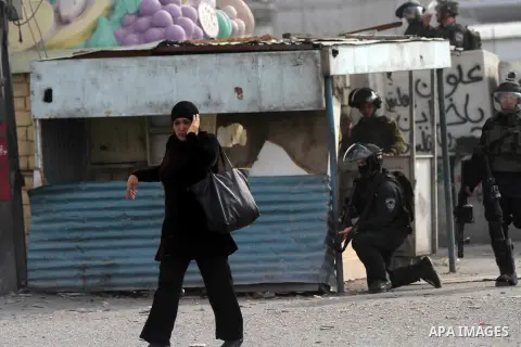 A Palestinian woman walks past members of Israeli security forces during clashes with Palestinian protesters following a protest against Israeli restrictions to Al-Aqsa Mosque in Jerusalem, at the Qalandia checkpoint nea...