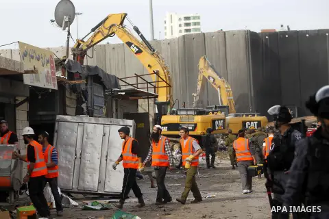 Israeli security forces stand guard while construction vehicles destroy Palestinian owned shops that were built without a permit in the Shuafat refugee camp in east Jerusalem, on December 3, 2014. Palestinian homes built...