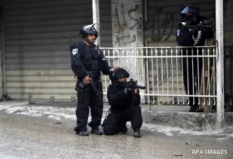 A member of Israeli security forces aims his gun at Palestinian protesters as others stand guard while construction vehicles destroy Palestinian owned shops that were built without a permit in the Shuafat refugee camp in...