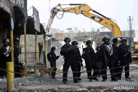 Israeli security forces stand guard while construction vehicles destroy Palestinian owned shops that were built without a permit in the Shuafat refugee camp in east Jerusalem, on December 3, 2014. Palestinian homes built...