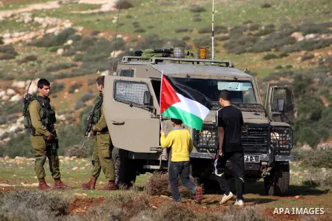 Palestinian children waving a Palestinian flag, walk past Israeli soldiers as they stand guard at an agricultural land in Salem village, near the West Bank city of Nablus, December 5, 2014. Many groves are effectively of...