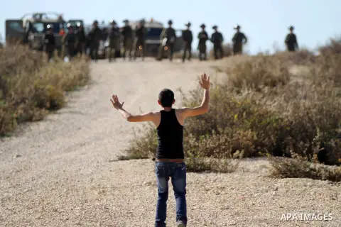 A Palestinian protesters gestures in front of Israeli security forces during clashes following a demonstration against Israel's controversial barrier, in the outskirts of the village of Bilin, near the West Bank city of...