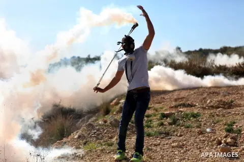 A Palestinian protester uses a slingshot to throw back a tear gas canister fired by Israeli security forces during clashes following a demonstration against Israel's controversial barrier, in the outskirts of the village...