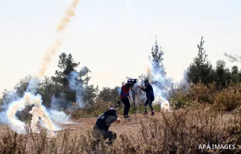 Palestinian media members take cover from tear gas fired by Israeli security forces during clashes with Palestinian protesters following a demonstration against Israel's controversial barrier, in the outskirts of the vil...