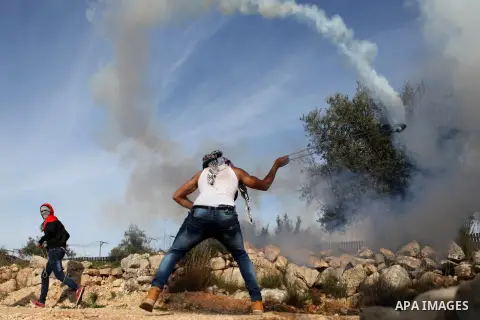 A Palestinian protester uses a slingshot to throw back a tear gas canister fired by Israeli security forces during clashes following a demonstration against Israel's controversial barrier, in the outskirts of the village...