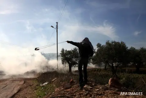 A Palestinian protester uses a slingshot to throw back a tear gas canister fired by Israeli security forces during clashes following a demonstration against Israel's controversial barrier, in the outskirts of the village...