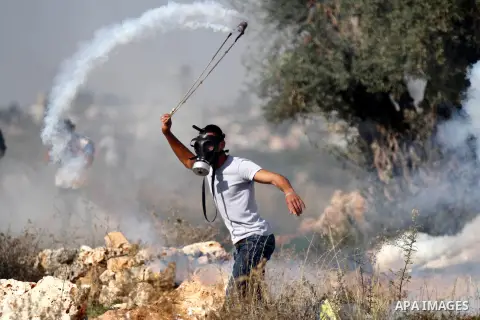 A Palestinian protester uses a slingshot to throw back a tear gas canister fired by Israeli security forces during clashes following a demonstration against Israel's controversial barrier, in the outskirts of the village...