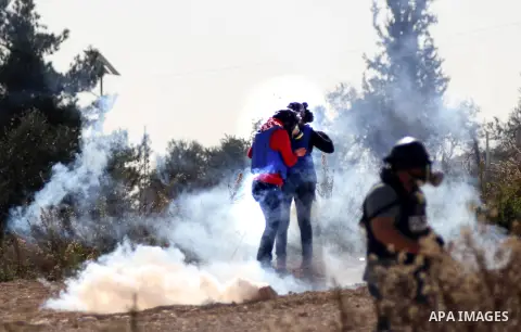 Palestinian media members take cover from tear gas fired by Israeli security forces during clashes with Palestinian protesters following a demonstration against Israel's controversial barrier, in the outskirts of the vil...