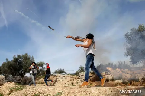 A Palestinian protester uses a slingshot to throw back a tear gas canister fired by Israeli security forces during clashes following a demonstration against Israel's controversial barrier, in the outskirts of the village...