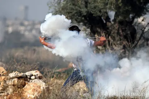 A Palestinian protester uses a slingshot to throw back a tear gas canister fired by Israeli security forces during clashes following a demonstration against Israel's controversial barrier, in the outskirts of the village...