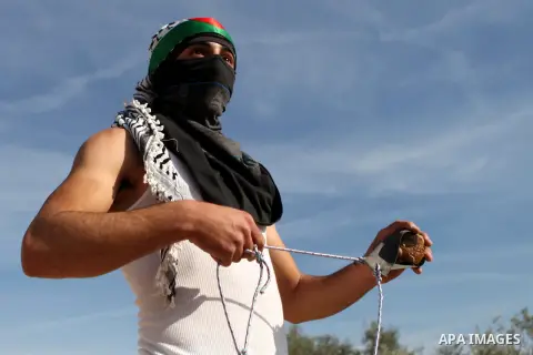 A Palestinian protester uses a slingshot to throw a stone towards Israeli security forces during clashes following a demonstration against Israel's controversial barrier, in the outskirts of the village of Bilin, near th...