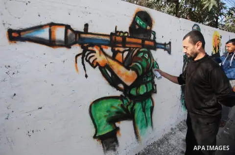 A Palestinian artist paints a mural on a wall marking the 27th anniversary of the Islamist movement's of Hamas founding at Nuseirat in the central of Gaza strip on December 11, 2014. Photo by Ashraf Amra
