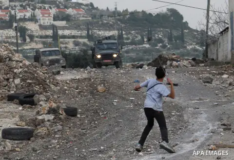 A Palestinian boy uses a slingshot to throw stones at Israeli security forces during clashes in a protest against the expropriation of Palestinian land by Israel following Friday prayers in the village of Kafr Qaddum, ne...