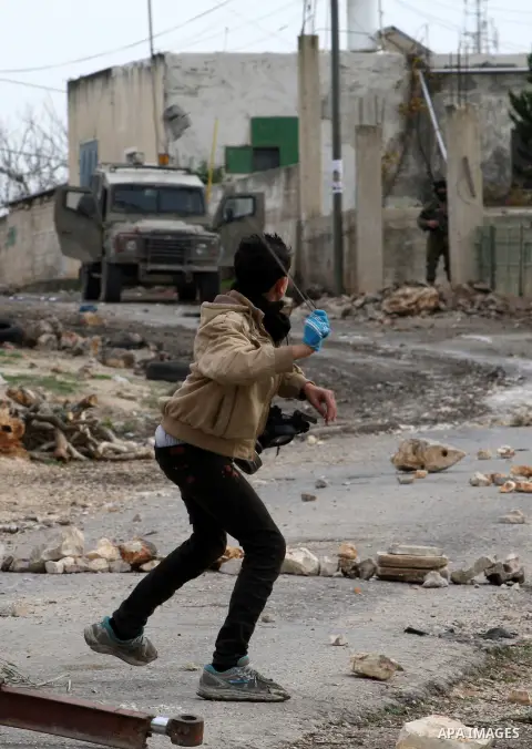 A Palestinian boy uses a slingshot to throw stones at Israeli security forces during clashes in a protest against the expropriation of Palestinian land by Israel following Friday prayers in the village of Kafr Qaddum, ne...