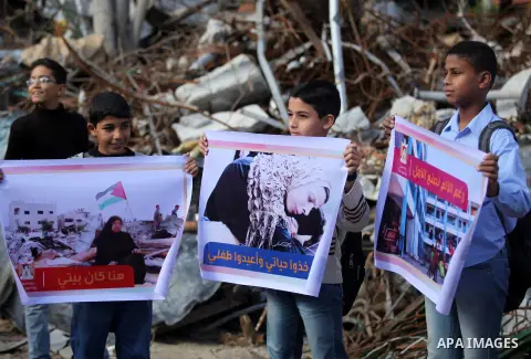 Palestinian children hold banners during a media conference organised by the ministry of women affairs in front of the Italian Complex, which was destroyed by Israeli air strike during the Israel-Gaza conflict, in Gaza c...