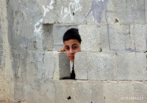 A Palestinian boy takes cover during clashes with Israeli security forces against the expropriation of Palestinian land by Israel following Friday prayers in the village of Kafr Qaddum, near Nablus, Dec. 19, 2014. Photo...