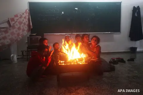 Palestinians warm themselves around a fire at a United Nations (UN) run school sheltering Palestinians, whose houses were destroyed in the 50- day-war Israeli last summer, during a winter storm in Beit Hanoun in the nort...