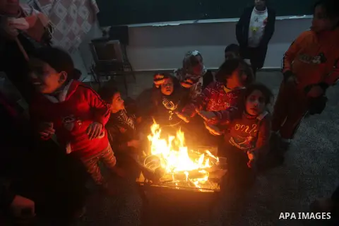 Palestinians warm themselves around a fire at a United Nations (UN) run school sheltering Palestinians, whose houses were destroyed in the 50- day-war Israeli last summer, during a winter storm in Beit Hanoun in the nort...