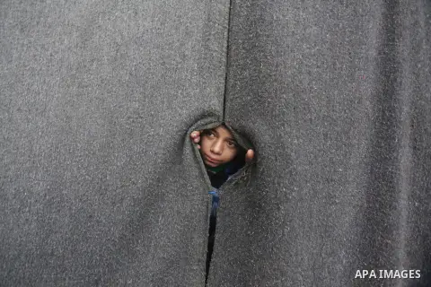 A Palestinian girl looks on behind a curtain at a United Nations (UN) run school sheltering Palestinians, whose houses were destroyed in the 50- day-war Israeli last summer, during a winter storm in Beit Hanoun in the no...