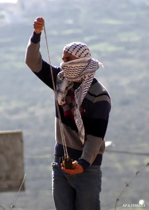 A Palestinian protester uses a slingshot to throw a stone towards Israeli security forces during clashes following a demonstration against the expropriation of Palestinian land by Israel in the village of Kfar Qaddum, ne...