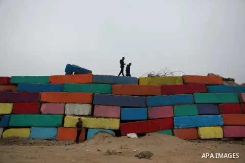 Palestinian walk on a big stone wall on January 25, 2015 that was painted by local artists at the sea port in Gaza City in an attempt to bring more vibrant colours to the city. Photo by Ashraf Amra
