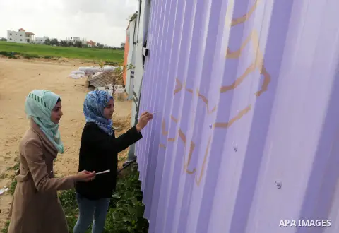 Palestinian girls paint a container of a family, which their house was destroyed by Israeli shelling during a 50-day conflict last summer, east if Khan Younis in the southern Gaza Strip, January 28, 2015. Dozens of prote...