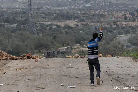 A Palestinian protester uses a sling shot to throw stones towards Israeli border policemen during clashes following a protest against closure of the village road, in the West Bank village of Azzun near Qalqilya February...