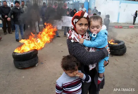 Smoke rises from burning tyres as Palestinians shout during a protest calling for reconstruction of their houses that witnesses said were destroyed by Israeli shelling during a 50-day war last summer, outside a United Na...