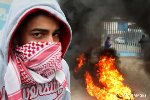 A Palestinian man standing near burning tyres takes part in a protest calling for reconstruction of houses that witnesses said were destroyed by Israeli shelling during a 50-day war last summer, outside a United Nations...