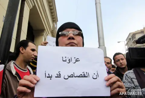 An Egyptian woman holds a placard with Arabic inscription reading 'We are consoled as retribution began' to denounce the killing of Egyptian Christians in Libya, outside the Coptic Cathedral of Saint Marcos, in Cairo, Eg...