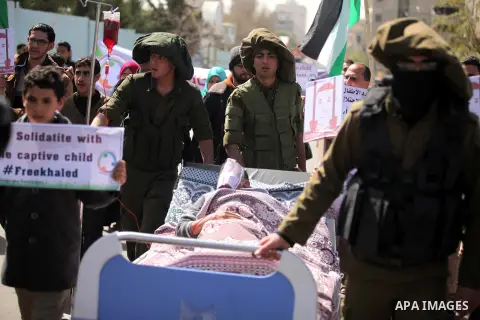 Palestinians enact a scene of Israeli soldiers pushes a boy lying in a bed in reference to Khaled al-Sheikh, a 14-years-old Palestinian boy jailed in an Israeli prison, during a rally calling for his release in Gaza City...