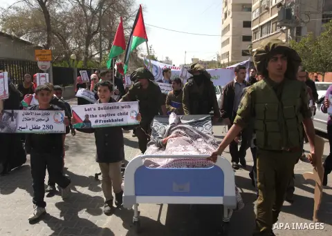 Palestinians enact a scene of Israeli soldiers pushes a boy lying in a bed in reference to Khaled al-Sheikh, a 14-years-old Palestinian boy jailed in an Israeli prison, during a rally calling for his release in Gaza City...