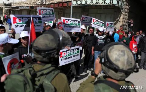 Palestinian demonstrators hold placards in front of Israeli soldiers during a protest demanding the reopening of Shuhada Street in the West Bank city of Hebron on February 27, 2015. Photo by Mamoun Wazwaz