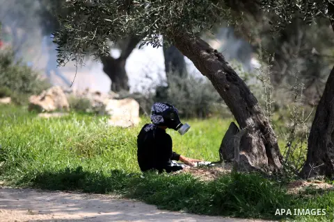 A Palestinian protester takes a shelter during clashes with Israeli security forces following a demonstration against Jewish settlements in the West Bank village of Bilin, west of Ramallah, February 27, 2015. Photo by Sh...