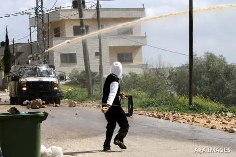 A Palestinian protester throws stones towards an Israeli military vehicle spraying a foul-smelling spray known as "skunk" during clashes in a protest against the expropriation of Palestinian land by Israel in the West Ba...