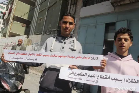 Palestinian youths hold banners during a protest against the power crisis in Gaza strip, in front of Electricity company, in Gaza city, on March 23, 2015. Photo by Mohammed Asad