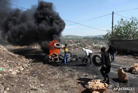 A Palestinian protester throws a tyre into a fire during clashes with Israeli security forces following a protest against the expropriation of Palestinian land by Israel in the West Bank village of Kafr Qaddum, near the...