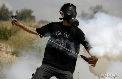 A masked Palestinian protester uses a slingshot to hurl back a tear gas canister fired by Israeli security forces during clashes following a demonstration marking Palestinian Prisoners' Day, in the West Bank village of B...