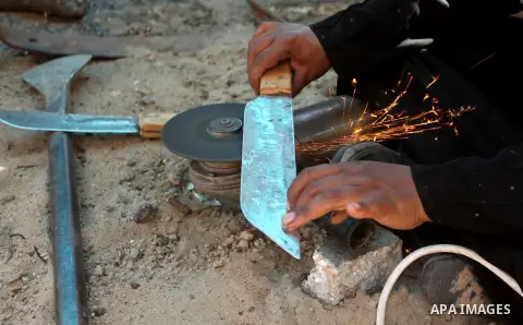 Aysha Ali, the wife of Ibraheem Mustafa, a 40-year-old Palestinian blacksmith, sharpens a handmade knife, at their small workshop in Gaza city on April 30, 2015. The ILO estimates that the 2014 conflict in Gaza raised un...