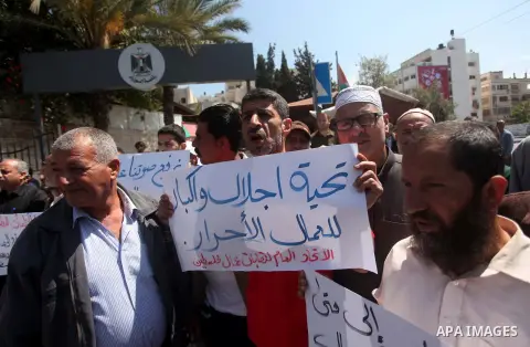 Palestinian workers hold banners during a protest demanding their rights in front of the Council of ministers headquarter, in Gaza city, on May 5, 2015. Photo by Ashraf Amra