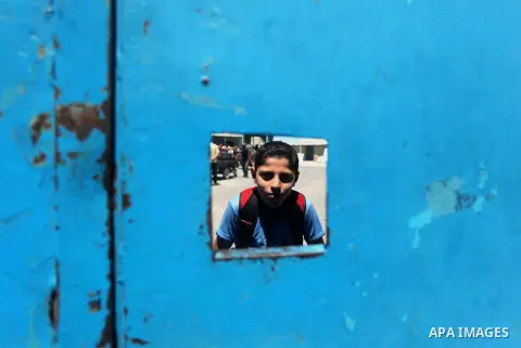 Palestinian child looks through at a window in school door during a protest to demand reconstruction of houses which were destroyed during the recent Israeli war, in front of the United Nations distribution center (UNRWA...