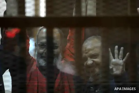 Egyptian Muslim Brotherhood top figure, Mohamed el-Beltagy flashes the four finger symbol known as "Rabaa" from behind the defendant's cage as the judge reads out the verdict sentencing him and more than 100 other defend...